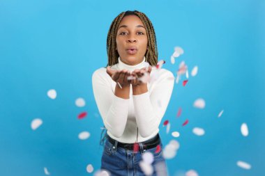 Studio portrait with blue background of an african woman looking at camera and blowing confetti