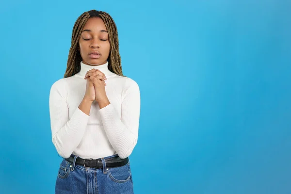 Studio portrait with blue background of an african woman with eyes closed and folded hands in prayer
