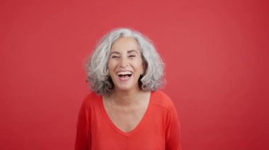Studio video with red background of a mature woman laughing