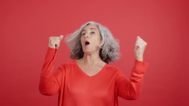 Студийное Видео Красном Фоне Зрелая Женщина Празднует Поднимая Кулаки — стоковое видео