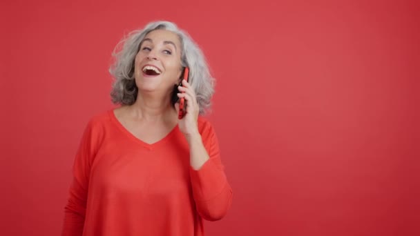 Studio Video Red Background Smiley Mature Woman Talking Mobile — Stockvideo