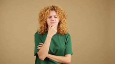 Studio video of a young woman with curly hair gesturing and looking up with doubtful expression