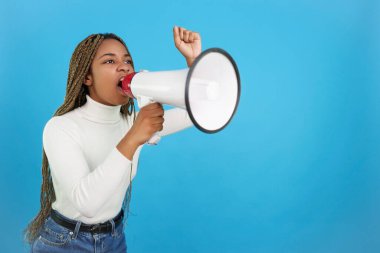 Studio portrait with blue background of a upset african woman protesting while shouting with a loudspeaker