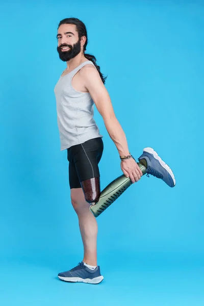 Vertical Studio portrait with blue background of a man with a prosthesis on his leg stretching his upper quadriceps