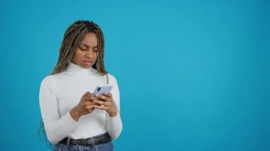 Video with blue background of an african woman with an expression of anger and incredulity looking at the phone