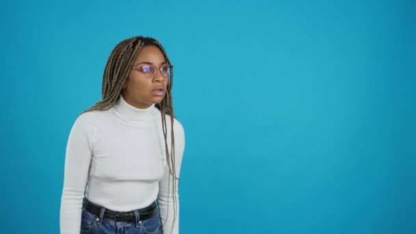 信じられないほどのカメラを見つめ眼鏡をかけたアフリカ人女性の青い背景を持つビデオ サイドビュー — ストック動画