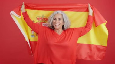 Studio video with red background of a happy mature woman raising a spanish national flag