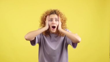 Studio video with yellow background of a beauty woman with curly hair gesturing with the hands on the face expressing dismay