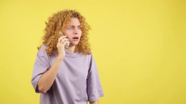 Studio video with yellow background of an angry woman with curly hair talk to the mobile phone