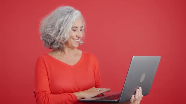 笑顔の成熟した女性が立っているとラップトップを使用しての赤い背景を持つスタジオビデオ — ストック動画