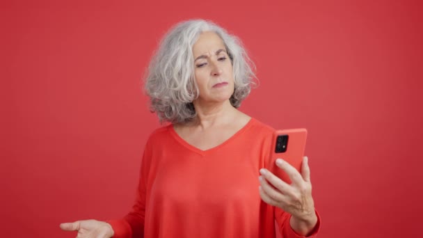 Студійне Відео Червоним Тлом Стурбованої Зрілої Жінки Допомогою Мобільного Телефону — стокове відео