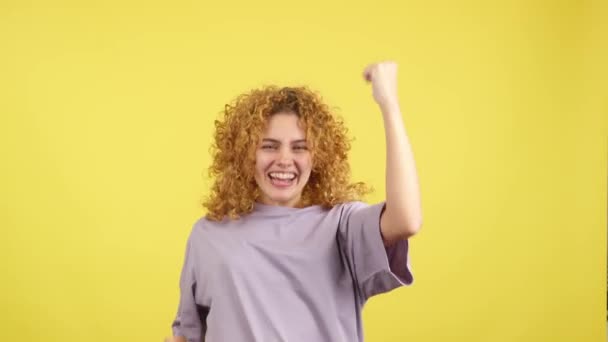 黄色の背景を持つスタジオビデオカメラを見ながらカール毛の女性の最初の人を祝う — ストック動画