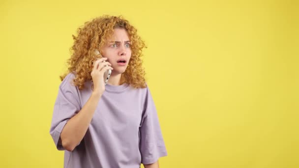 携帯電話に巻き毛の話と怒っている女性の黄色の背景を持つスタジオビデオ — ストック動画