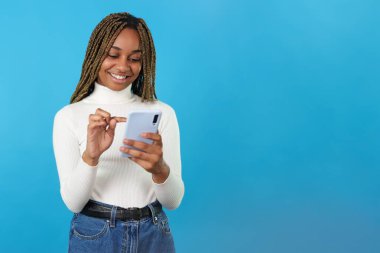 Studio portrait with blue background of an african smiling woman using the mobile phone