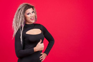 Transgender person with make up gesturing approval raising thumb up in studio with red background