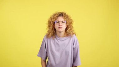 Studio video with yellow background of a young woman taking off her glasses to see far away while looking at camera