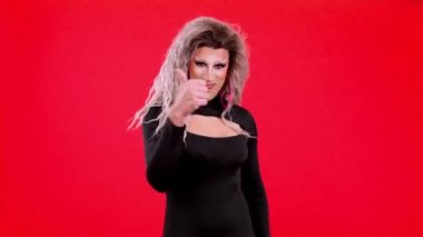 Transgender person with make up gesturing approval raising thumb up in studio with red background