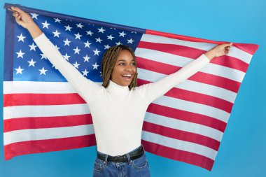 Studio portrait with blue background of a happy african woman raising an American flag