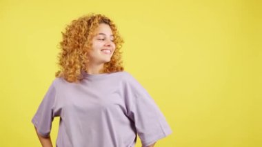 Studio video with yellow background of a young woman with curly hair pointing smiling to the side