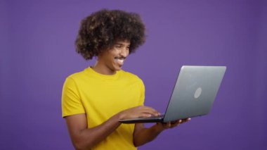 Happy african man wit curly hair standing and using a laptop in studio