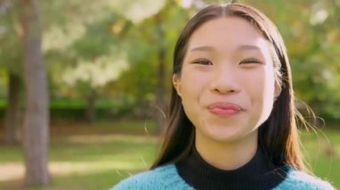 Slow motion video of a smiling asian woman looking at camera in a park