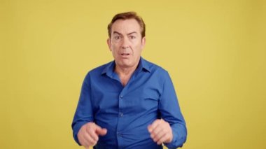 Mature man gesturing with the hands in fear in studio with yellow background