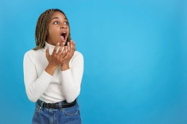 Studio portrait with blue background of an african woman staring into space from the side in surprise