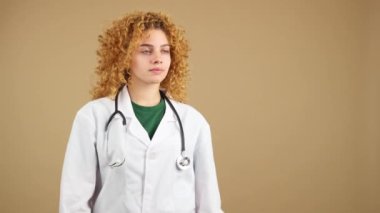 Studio video of a young serious female doctor with curly hair in lab coat with crossed arms, looking to copy space