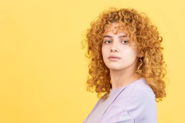 Studio image with yellow background of a beauty woman with curly hair turning to look at the camera