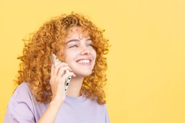 Studio photo with yellow background of a beauty and happy woman with curly hair talking to the mobile