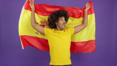 Happy african man with curly hair raising a spanish national flag in studio