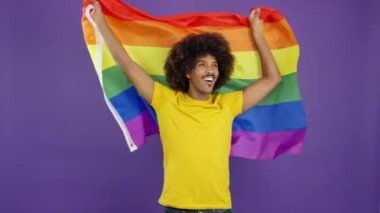Happy african man raising a lgbt rainbow flag while looking at the camera in studio