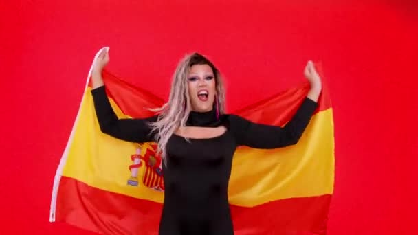 官能的なトランスジェンダーの人ドレスとしてドラッグクイーン提起スペイン語フラグでスタジオで赤の背景 — ストック動画