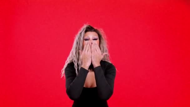 トランスジェンダー人ドレスとしてドラッグクイーン吹いてキス見ますカメラでスタジオでともに赤の背景 — ストック動画