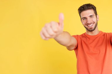 Happy caucasian man gesturing agreement raising a thumb up in studio with yellow background