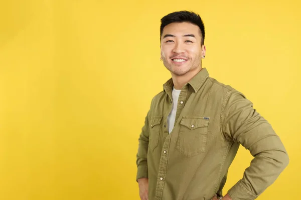 Handsome chinese man standing smiling at the camera in studio with yellow background