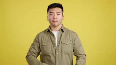 Serious chinese man standing with crossed arms and looking at camera in studio with yellow background