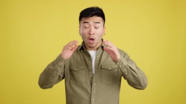 Surprised chinese man looking at the camera gesturing in studio with yellow background