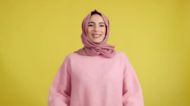 Happy muslim woman laughing in studio with yellow background