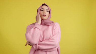 Sıkıcı Müslüman kadın sarı arka planla stüdyoda dikiliyor ve başka tarafa bakıyordu.