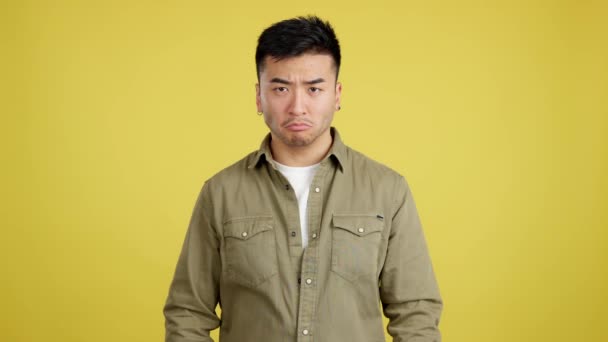 黄色の背景を持つスタジオでカメラを見ながら中国人男が怒りの表情で腕を横断 — ストック動画