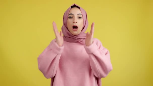 驚くべきイスラム教徒の女性でヒジャーブ見ますザ カメラでスタジオで黄色の背景 — ストック動画