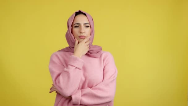 忧心忡忡的穆斯林女人 带着沉思的表情望着别处 在有黄色背景的工作室里 — 图库视频影像
