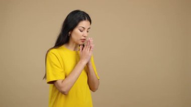 Caucasian woman praying with folded hands looking down in studio with brown background