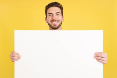 Happy caucasian man smiling while holding a blank panel in studio with yellow background