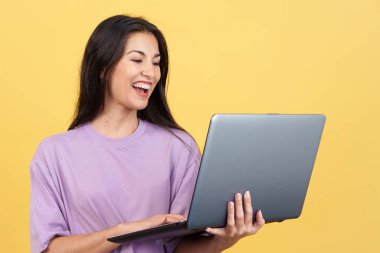 Caucasian woman smiling while using a laptop in studio with yellow background