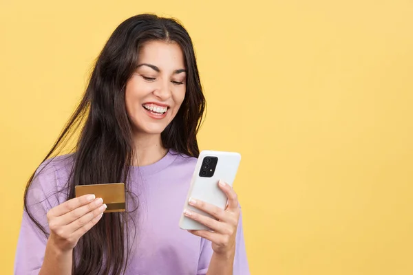 Happy woman using the mobile and card to shopping online in studio with yellow background