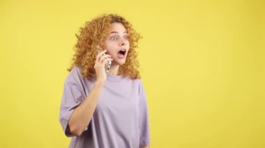 Stüdyo videosu, sarı arka planda kıvırcık saçlı bir kadının cep telefonuyla konuşurken ağzını açması.