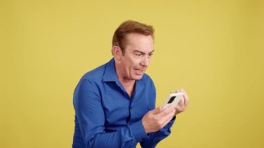 Mature man arguing during a video call with mobile phone in studio with yellow background