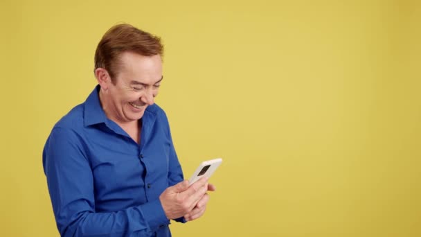 Happy Ώριμος Άνθρωπος Κοιτάζοντας Κινητό Τηλέφωνο Στο Στούντιο Κίτρινο Φόντο — Αρχείο Βίντεο